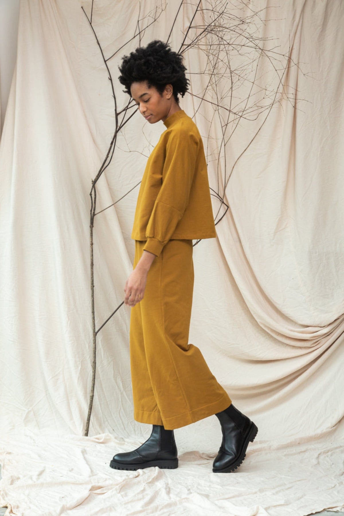 Person wearing a mustard yellow outfit standing against a neutral background