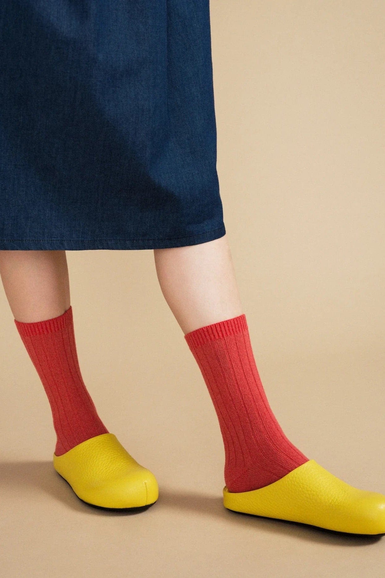 Person wearing red socks and yellow shoes on a beige background